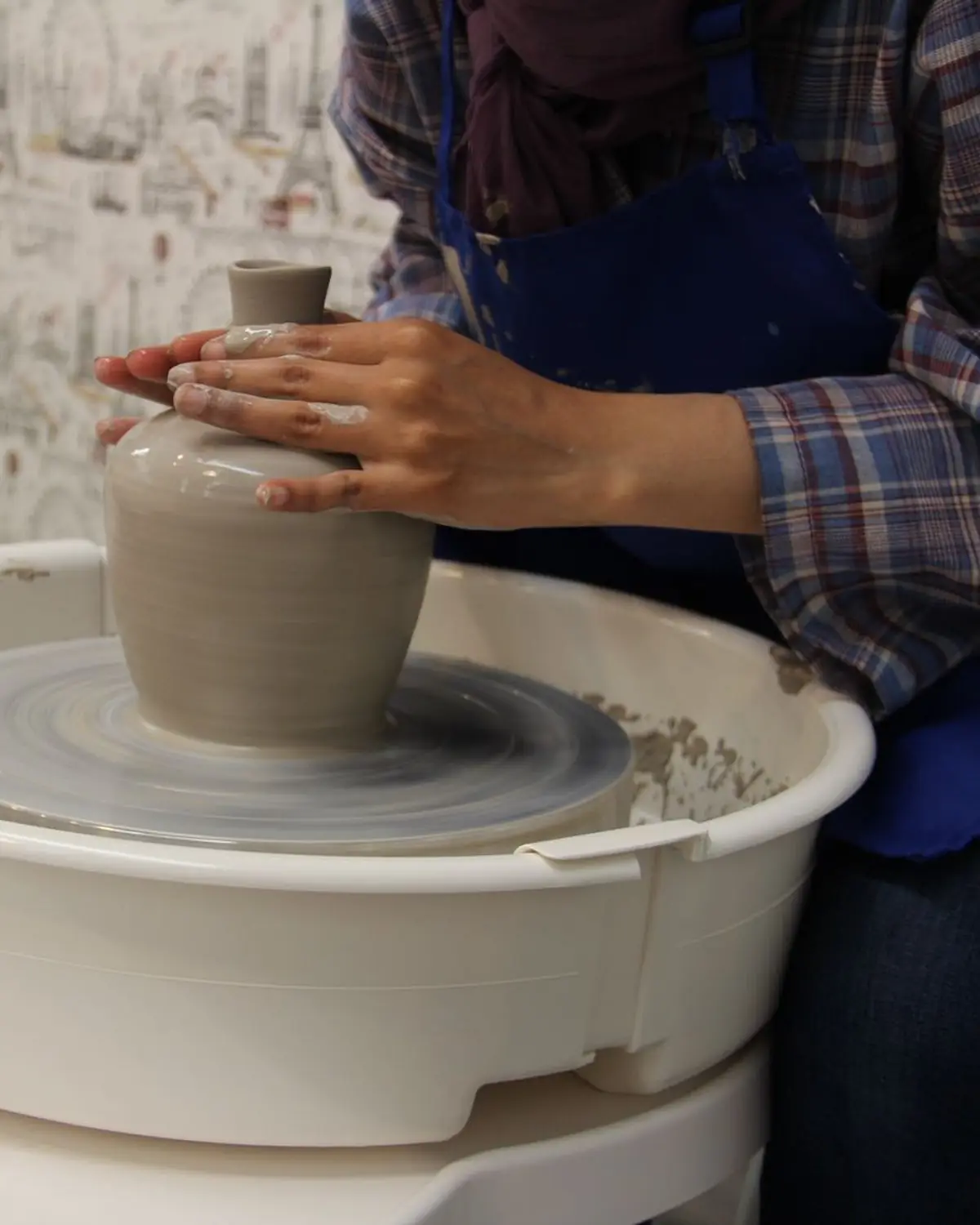 Hände formen eine schlanke Vase aus grauem Ton auf der Töpferscheibe